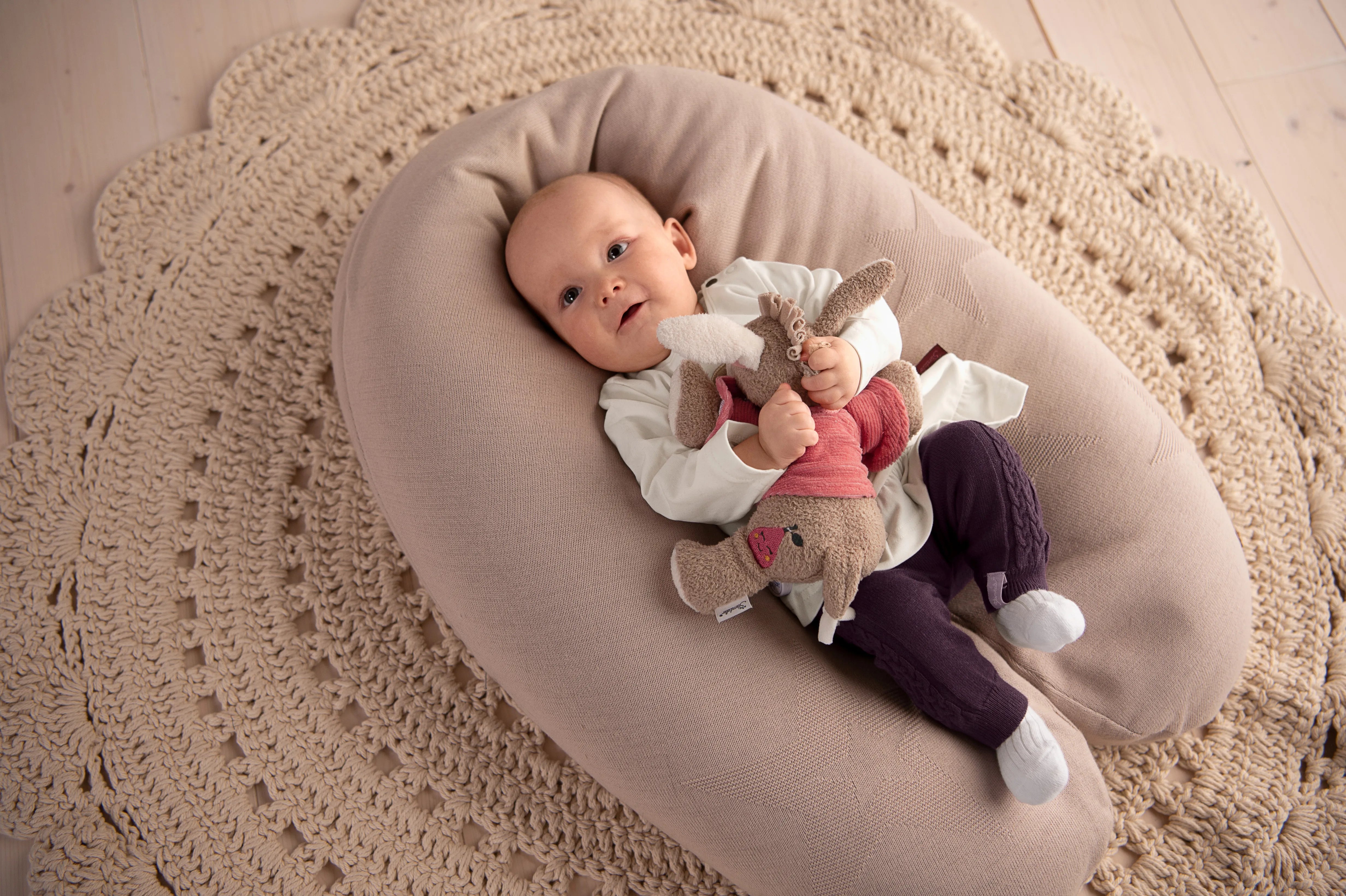 Lächelndes Baby in einem Nestchen liegend mit einem Kuscheltier in der Hand